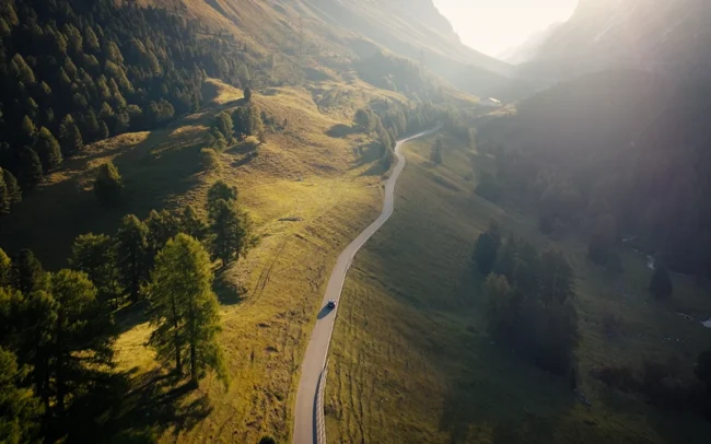 Drone shot of a AUDI Q6 e-tron driving up a Swiss mountain pass in golden morning light.
