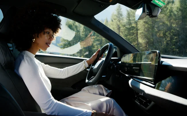 A beautiful black woman dressed in white sitting in an AUDI Q6 e-tron looking at the car's huge display.