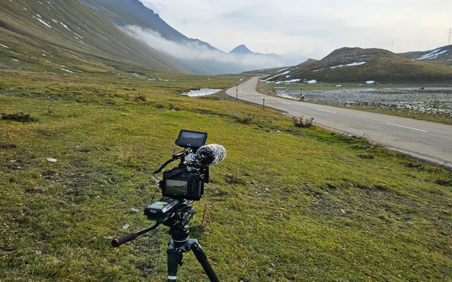 A camera on a tripod next to a street on a Swiss mountain pass.