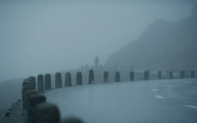 A foggy mountain road with the silhouette of a tiny cyclist all the way in the back.