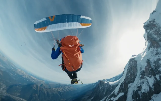 Insta360 angle of Elisa Deutschmann paragliding from a snowy mountain.