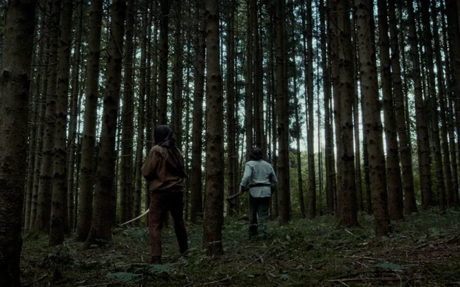 Wide shot of two hunters who are looking for the witch in a dense forest.