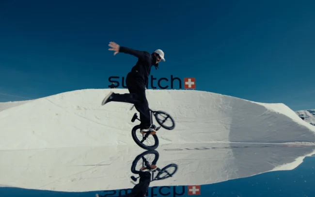 BMX rider dancing with his bike standing on a mirror in the mountains full of snow.