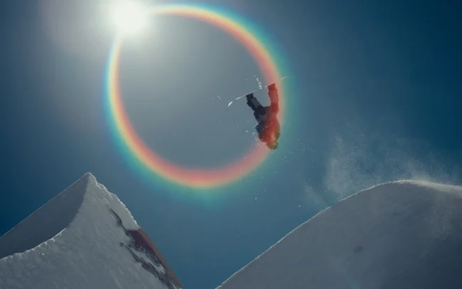 Snowboarder flying through artistic rainbow flare.