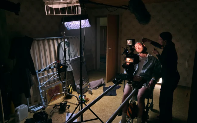 A candid behind-the-scenes photo of the Holy Moly Films production crew setting up a moody lit interrogation scene in a cellar.