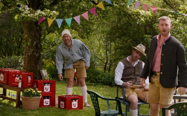 A seamless post-production VFX composite film still showing five cloned versions of Jonny Balchin interacting as different village characters within the same frame.