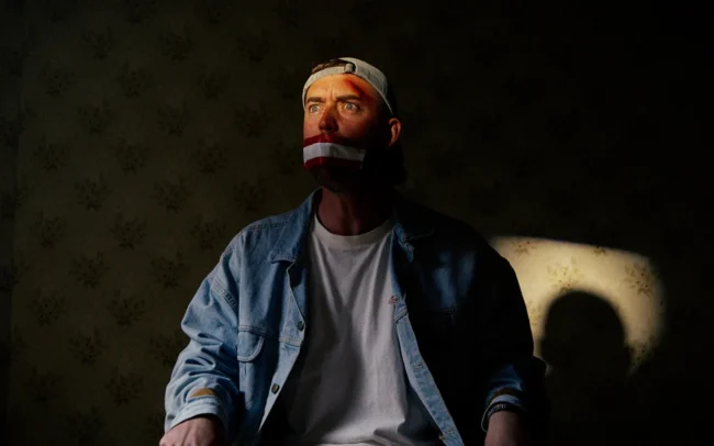 A dramatic and moody lit cinematic still of Jonny Balchin being kidnapped by Austrians for his latest sketch together with Imanuel Thallinger and Holy Moly films.