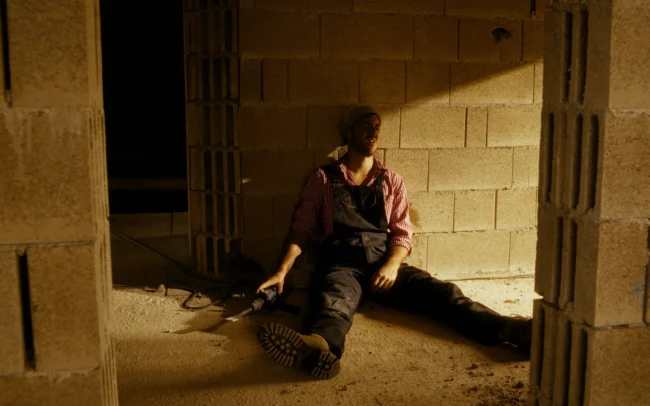 Austrian Kiwi construction worker sitting exhausted against a concrete wall on set during the comedy skit filming produced by Holy Moly Films.