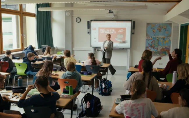 Wide shot of a bright Austrian secondary school classroom at HIB Saalfelden during the filming of a comedy sketch by Holy Moly Films.